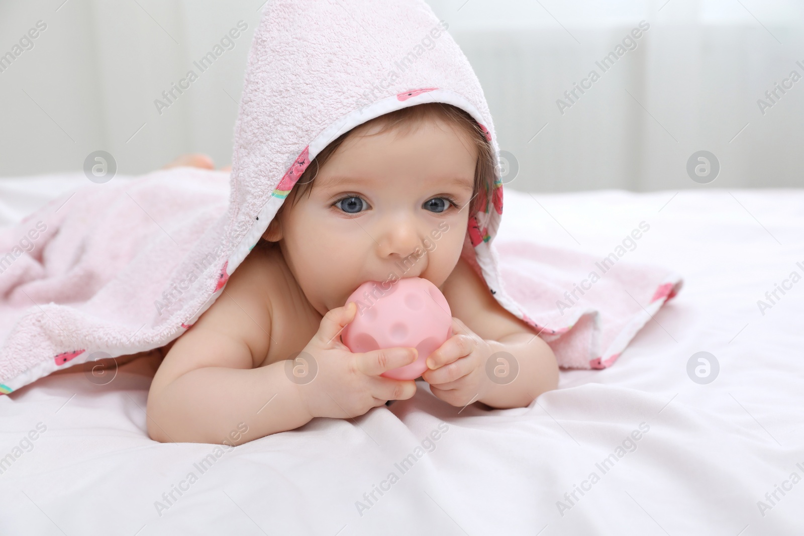 Photo of Cute little baby nibbling toy in hooded towel after bathing on bed at home