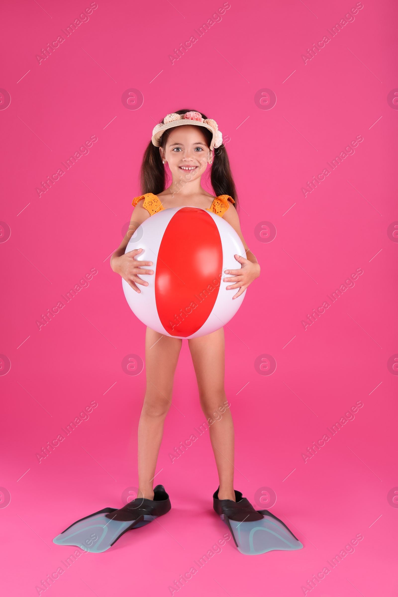 Photo of Cute little child in beachwear with bright inflatable ball on pink background