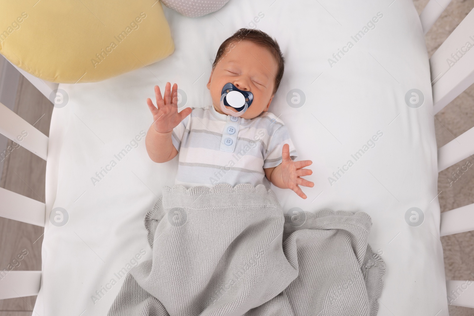 Photo of Cute newborn baby with pacifier sleeping under blanket in crib, top view. Bedtime