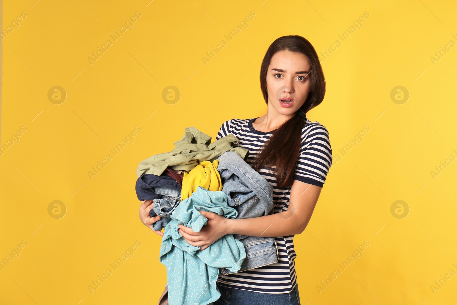 Photo of Emotional young woman holding pile of dirty laundry on color background