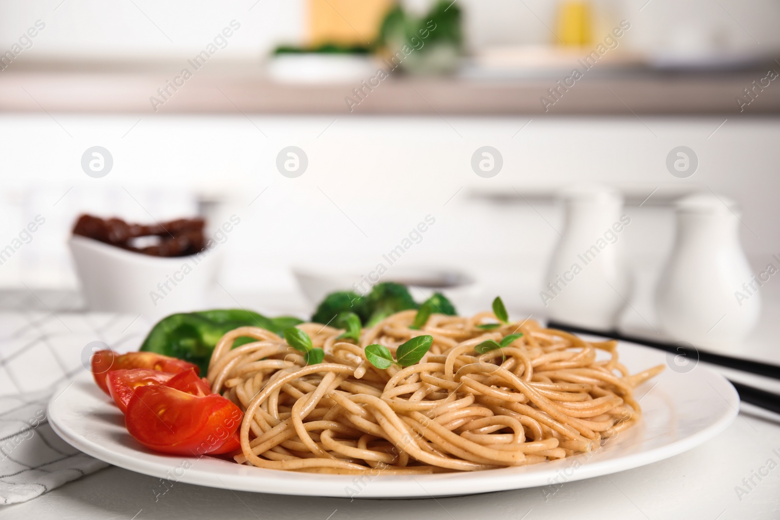 Photo of Plate of tasty buckwheat noodles with fresh vegetables on white kitchen table