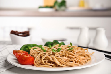 Plate of tasty buckwheat noodles with fresh vegetables on white kitchen table