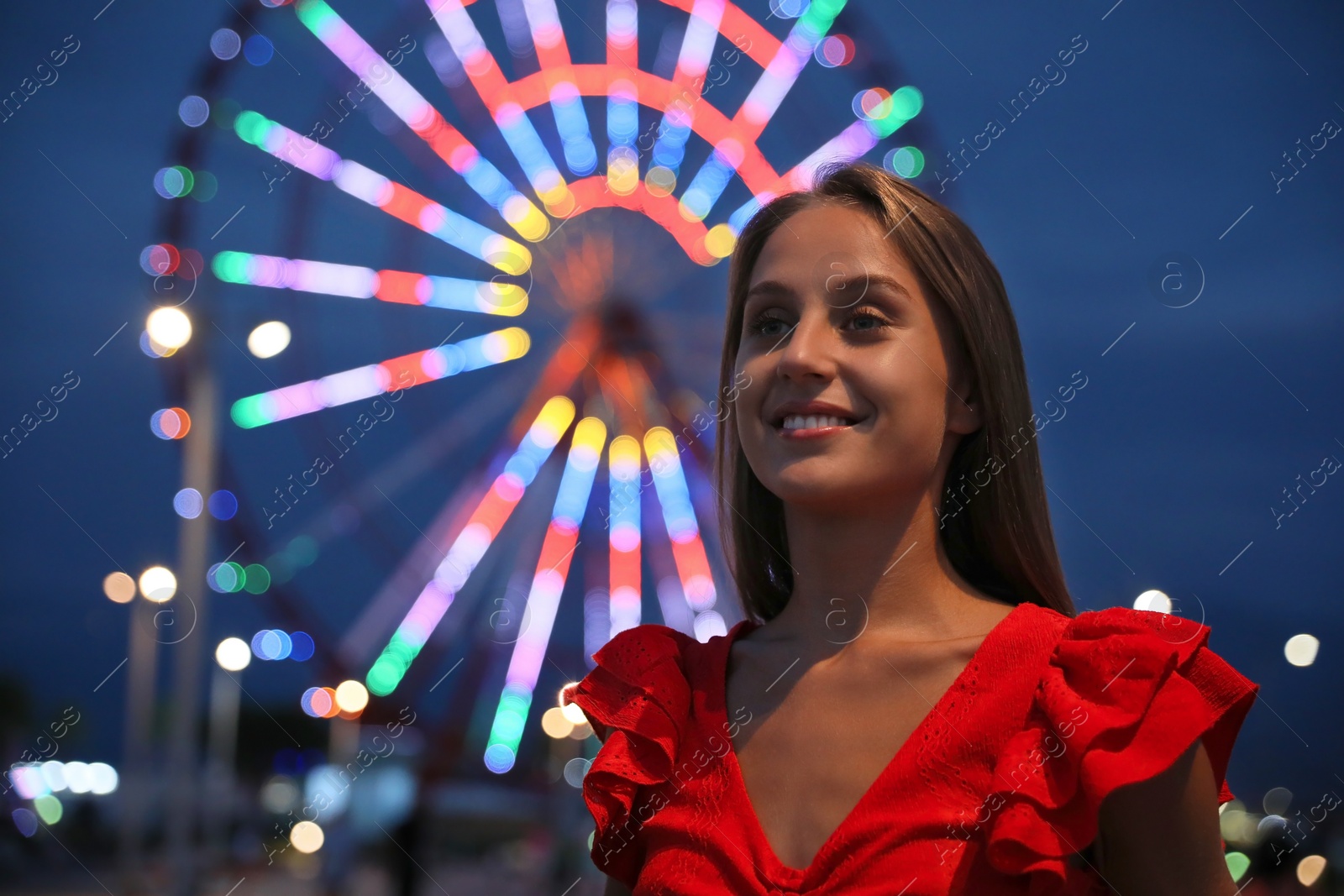 Photo of Beautiful young woman against glowing Ferris wheel in amusement park, space for text