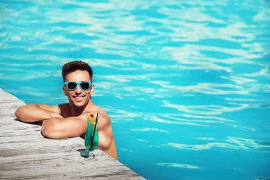 Image of Happy young man with cocktail in swimming pool