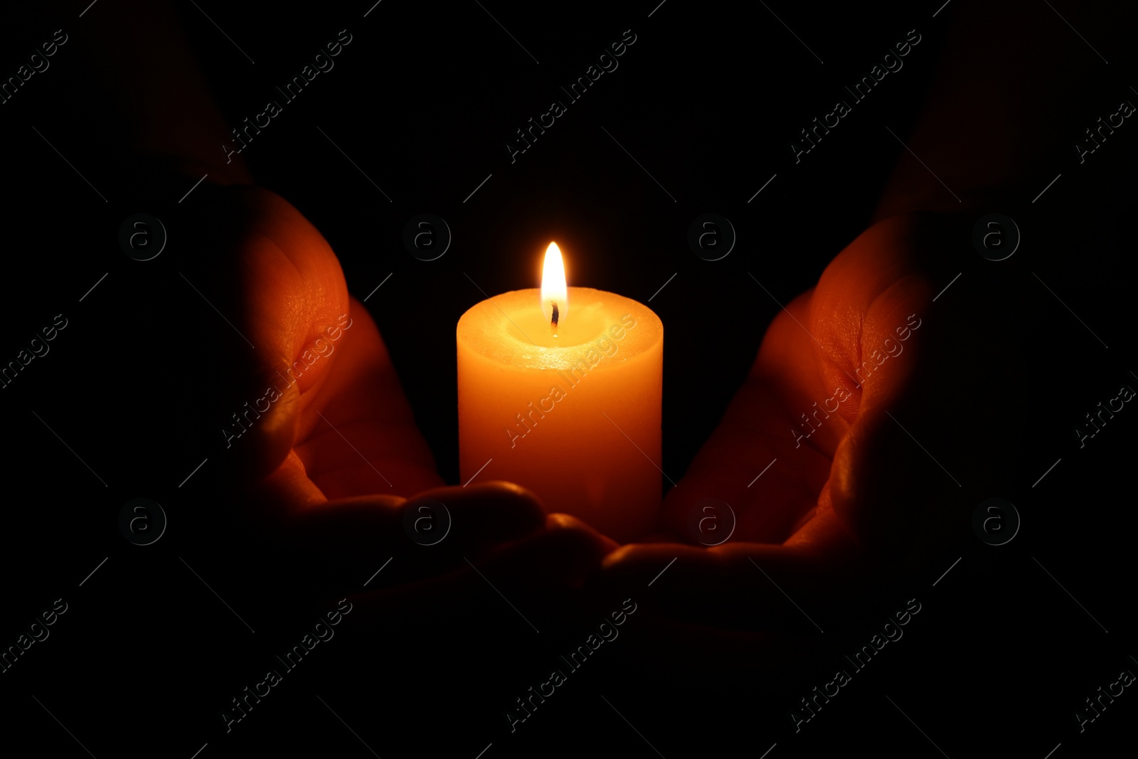 Photo of Woman holding burning candle in hands on black background, closeup