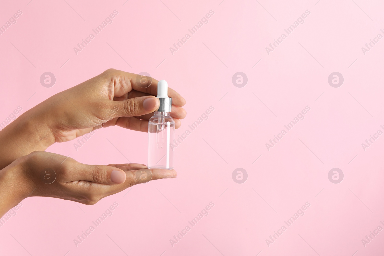 Photo of Woman with bottle of cosmetic serum on pink background, closeup. Space for text