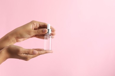 Woman with bottle of cosmetic serum on pink background, closeup. Space for text