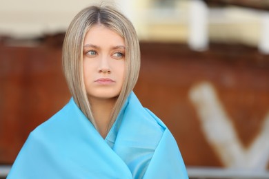Sad woman wrapped in Ukrainian flag against blurred background. Space for text