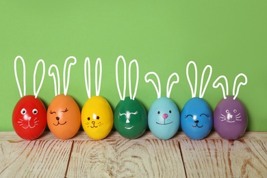Image of Colorful eggs as Easter bunnies on white wooden table against green background
