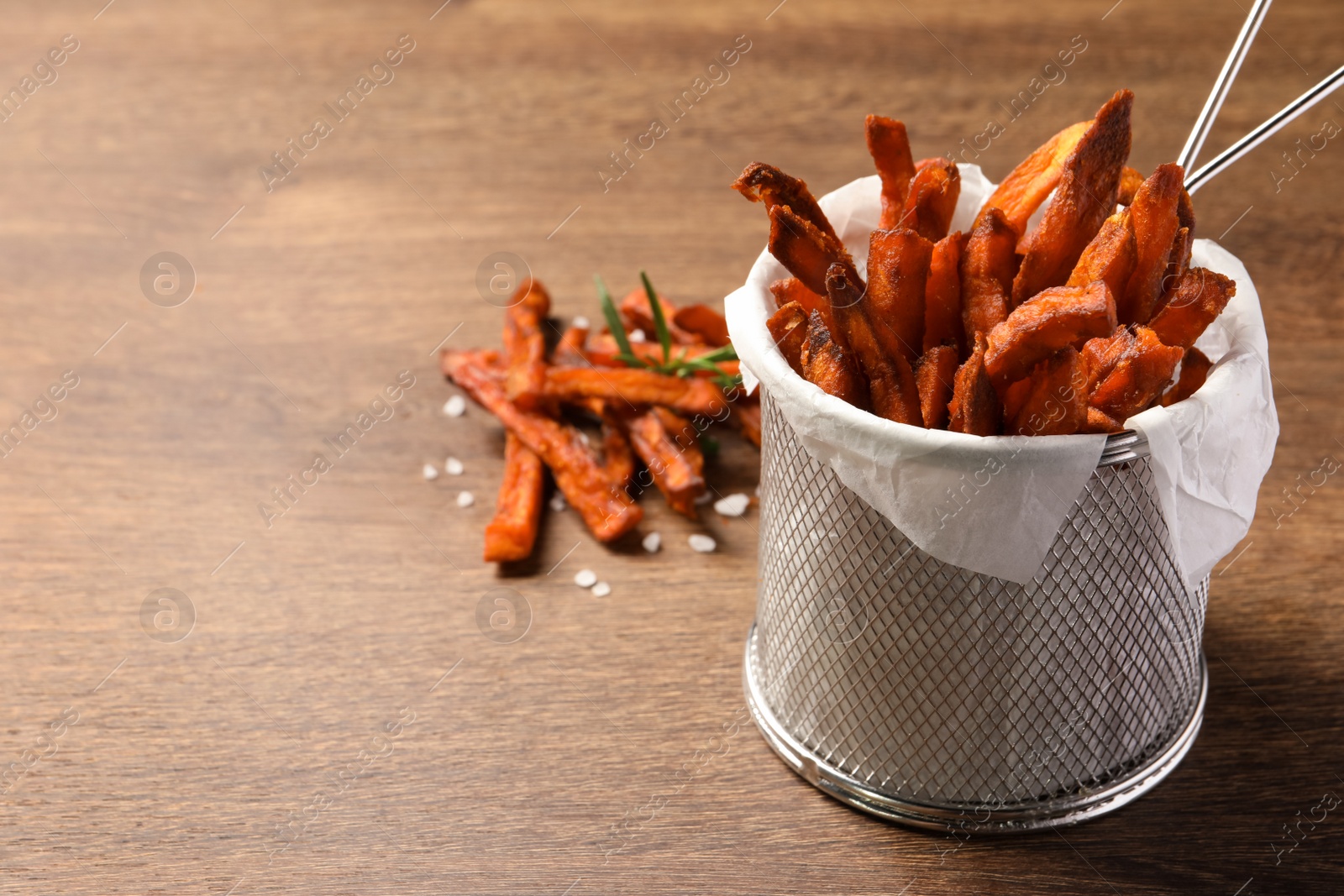 Photo of Frying basket with sweet potato fries on wooden table, closeup. Space for text