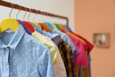 Different child's clothes hanging on rack indoors, closeup
