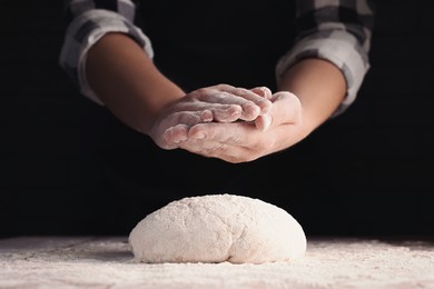 Photo of Man making dough at table against black background, closeup