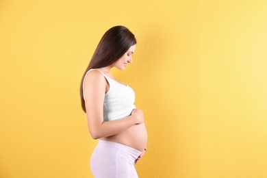 Photo of Beautiful pregnant woman holding hands on belly against color background. Space for text