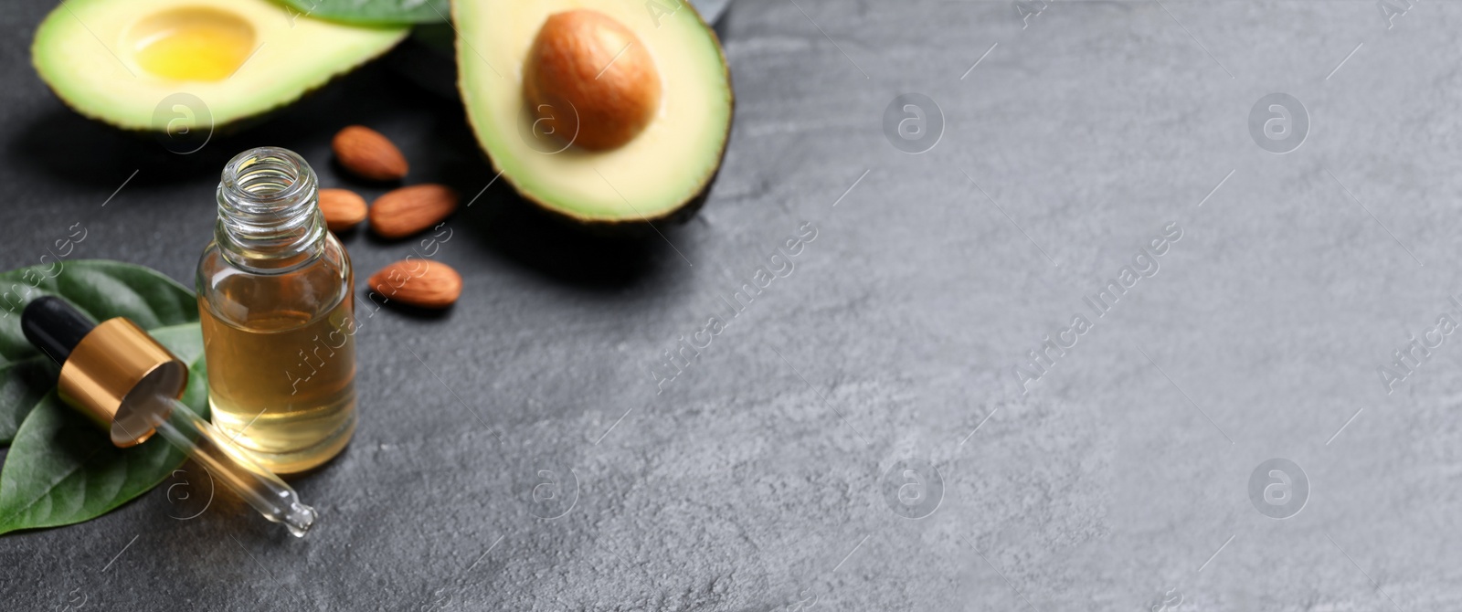 Photo of Essential oil, avocado and almonds on black table. Space for text