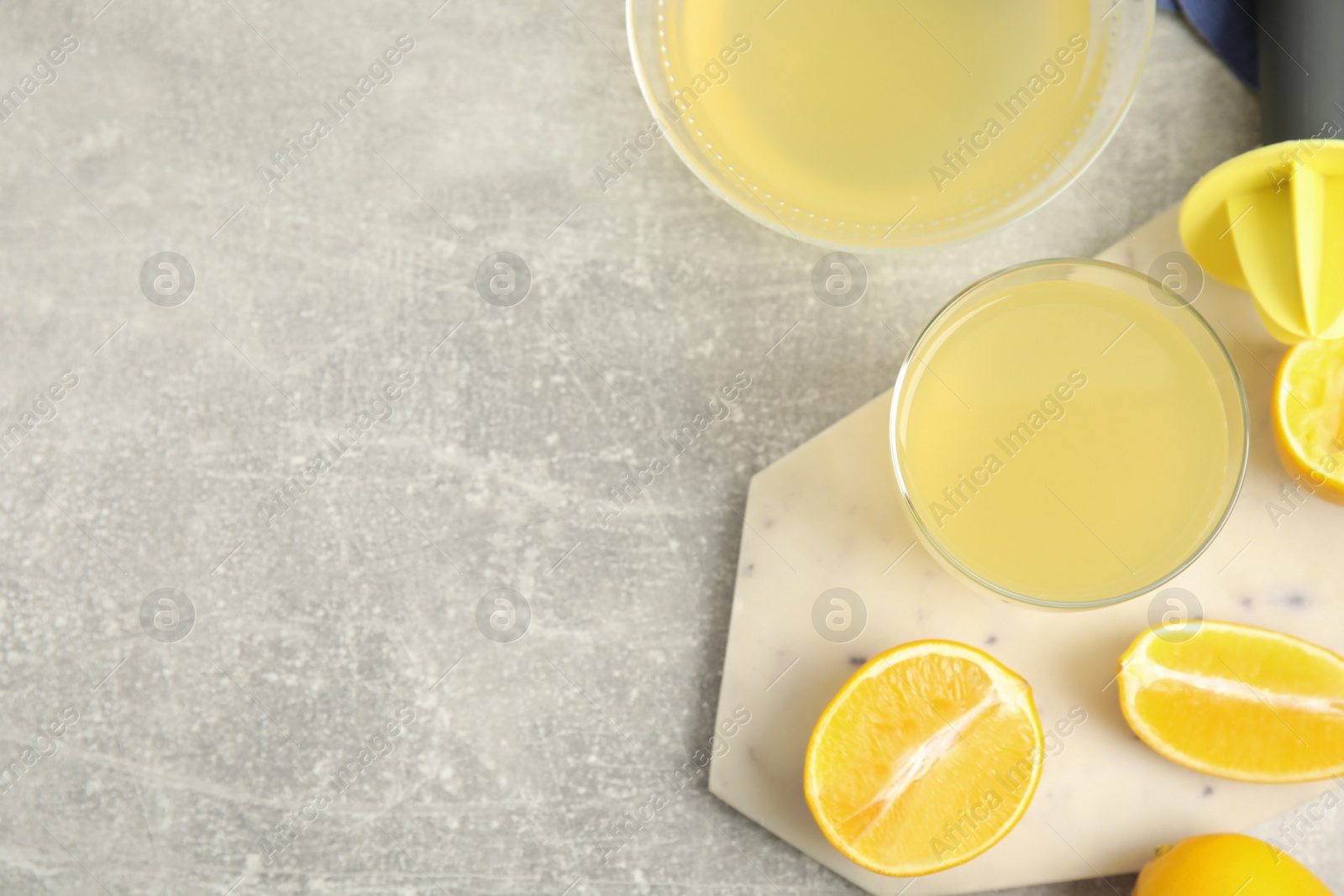 Photo of Freshly squeezed lemon juice on grey marble table, flat lay. Space for text