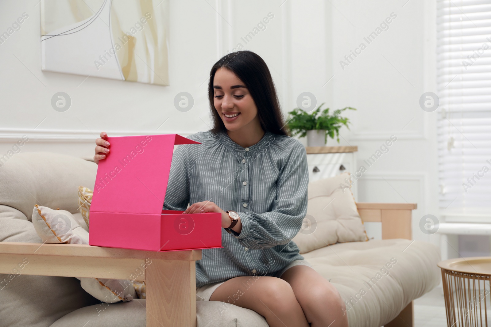 Photo of Happy young woman opening parcel at home. Internet shopping