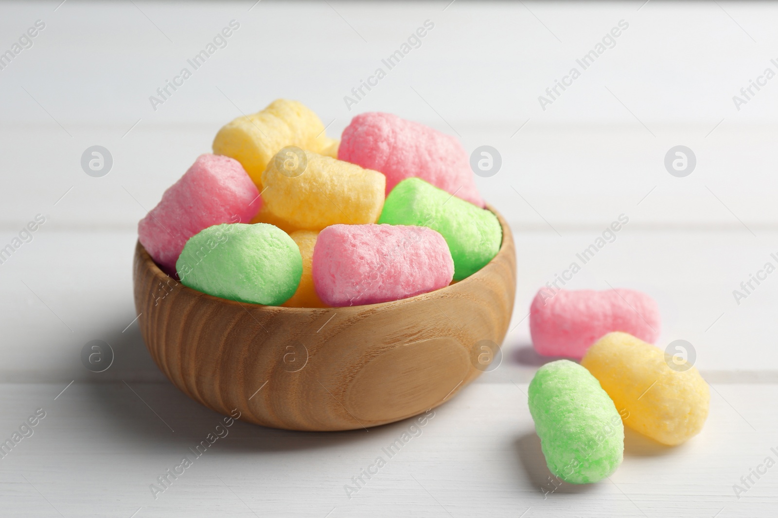 Image of Bowl with colorful corn puffs on white wooden table, closeup