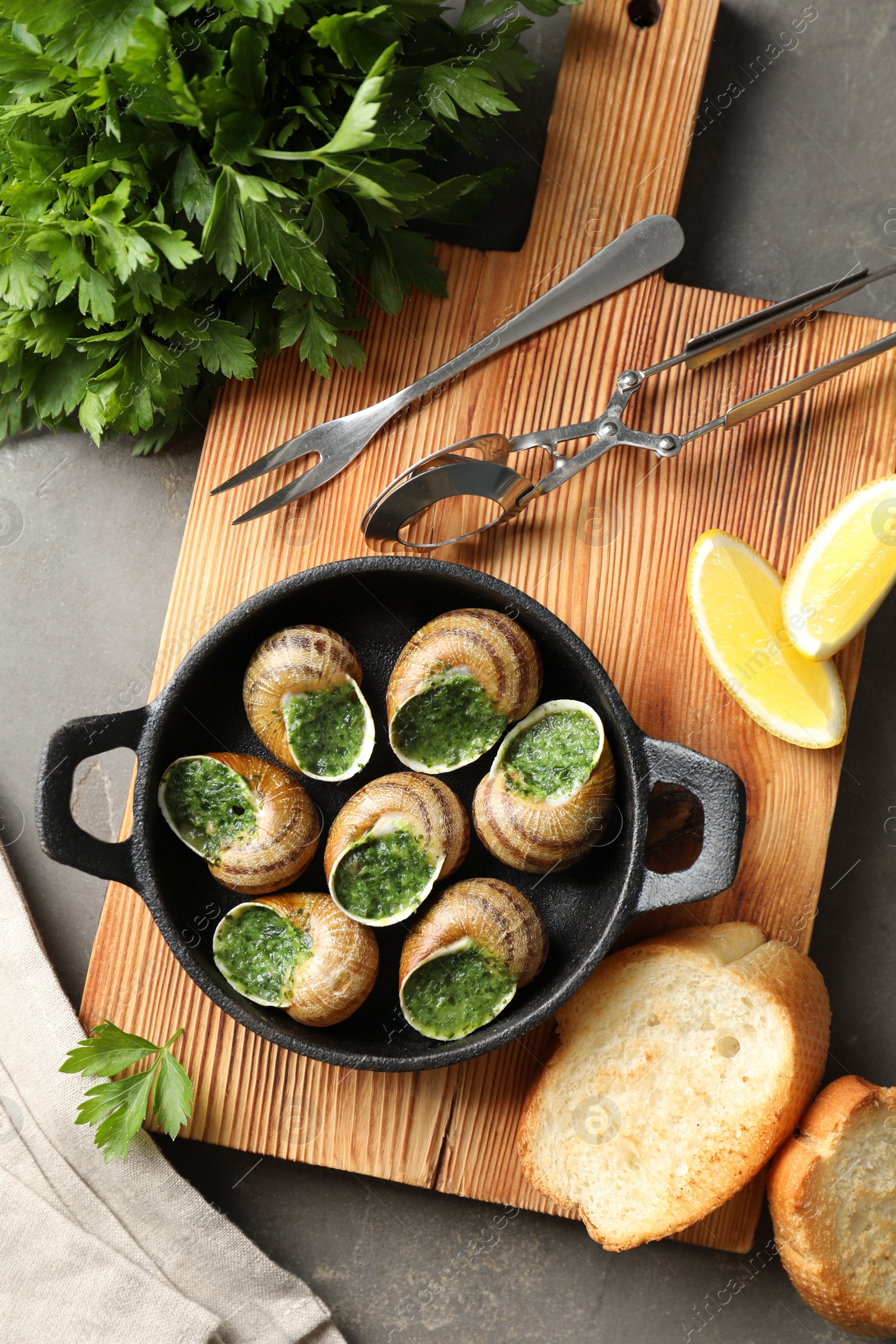 Photo of Delicious cooked snails in baking dish served on grey textured table, flat lay