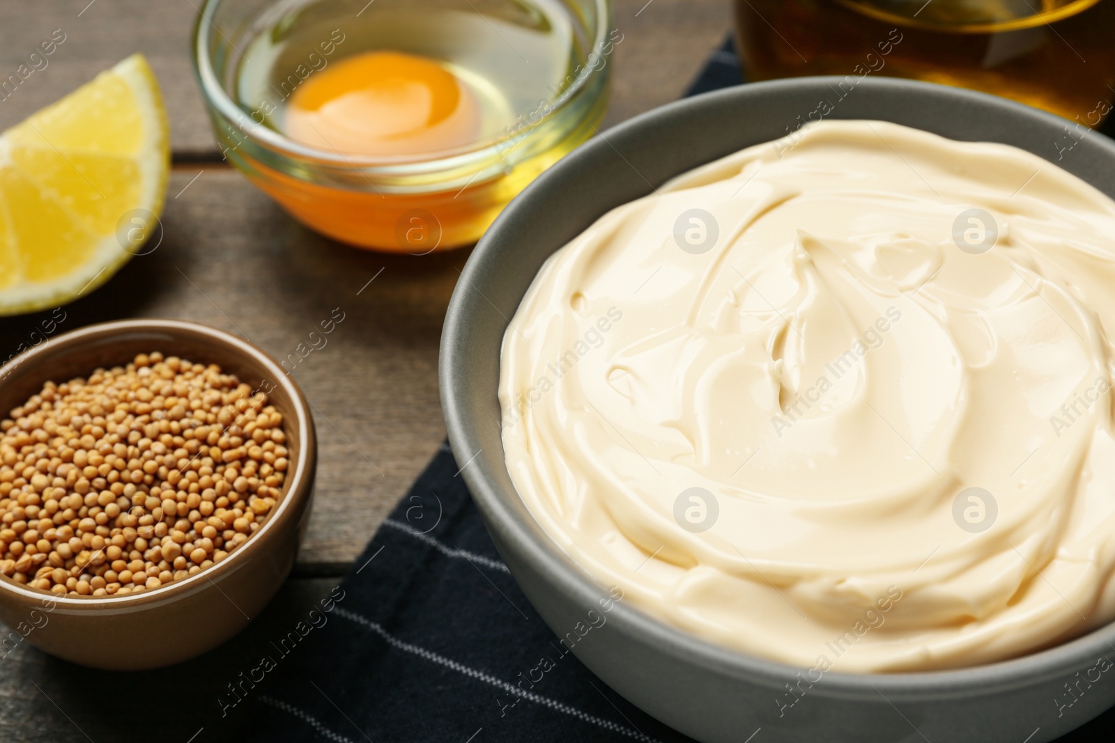 Photo of Bowl with fresh mayonnaise and ingredients on wooden table, closeup