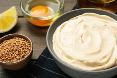 Photo of Bowl with fresh mayonnaise and ingredients on wooden table, closeup