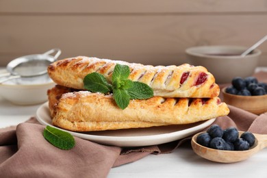 Photo of Fresh tasty puff pastry with sugar powder, mint and blueberries on white wooden table
