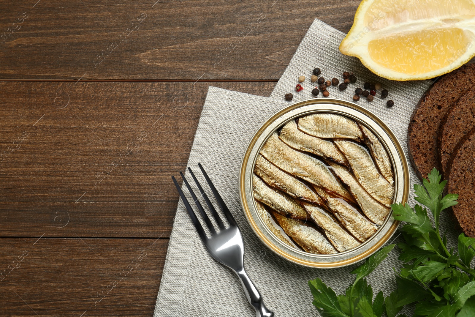 Photo of Tin can with tasty sprats served on wooden table, flat lay. Space for text