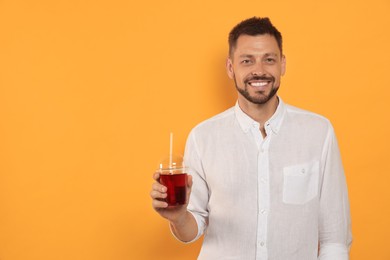 Man holding plastic cup of delicious juice on orange background, space for text