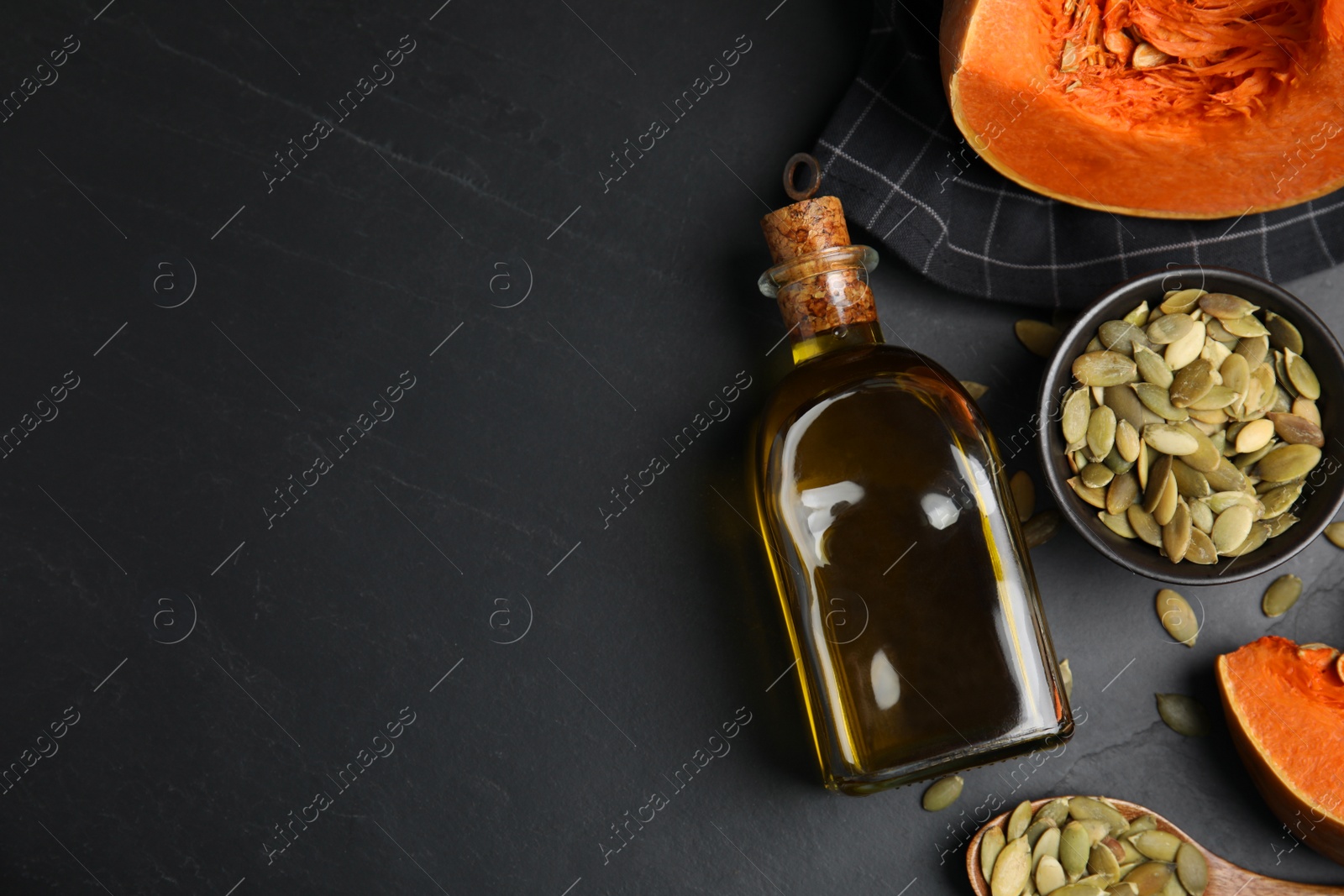 Photo of Glass bottle of oil with cut pumpkin and seeds on black table, flat lay. Space for text