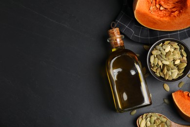 Photo of Glass bottle of oil with cut pumpkin and seeds on black table, flat lay. Space for text