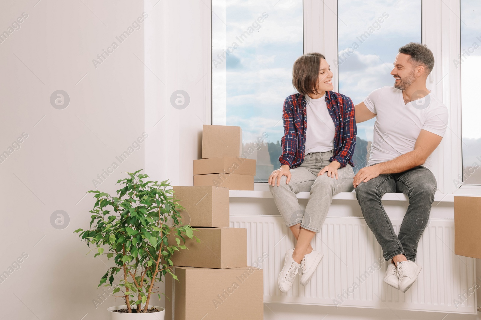 Photo of Happy couple sitting on windowsill in new apartment. Moving day