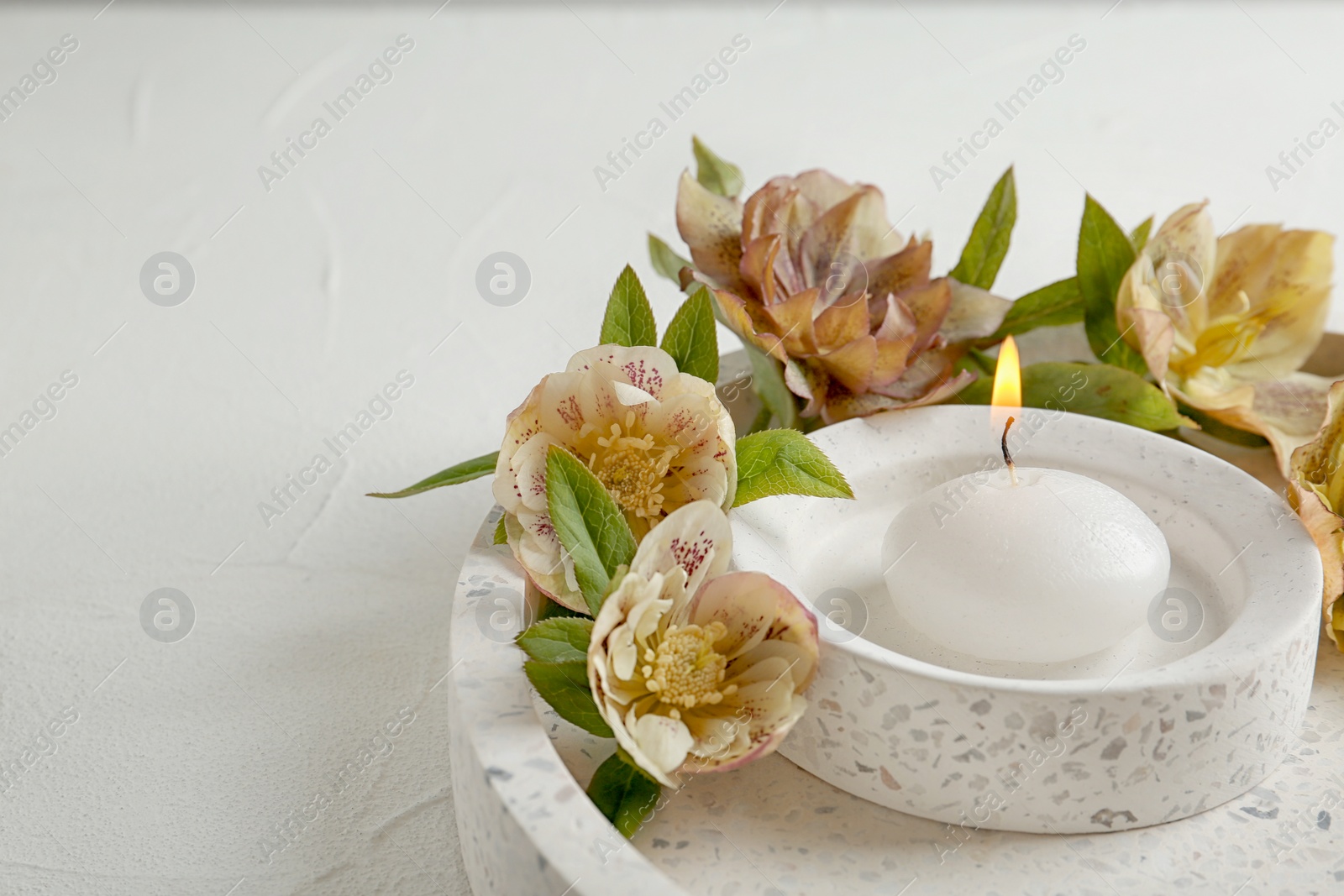 Photo of Stylish tender composition with burning candle and flowers on tray, space for text. Cozy interior element