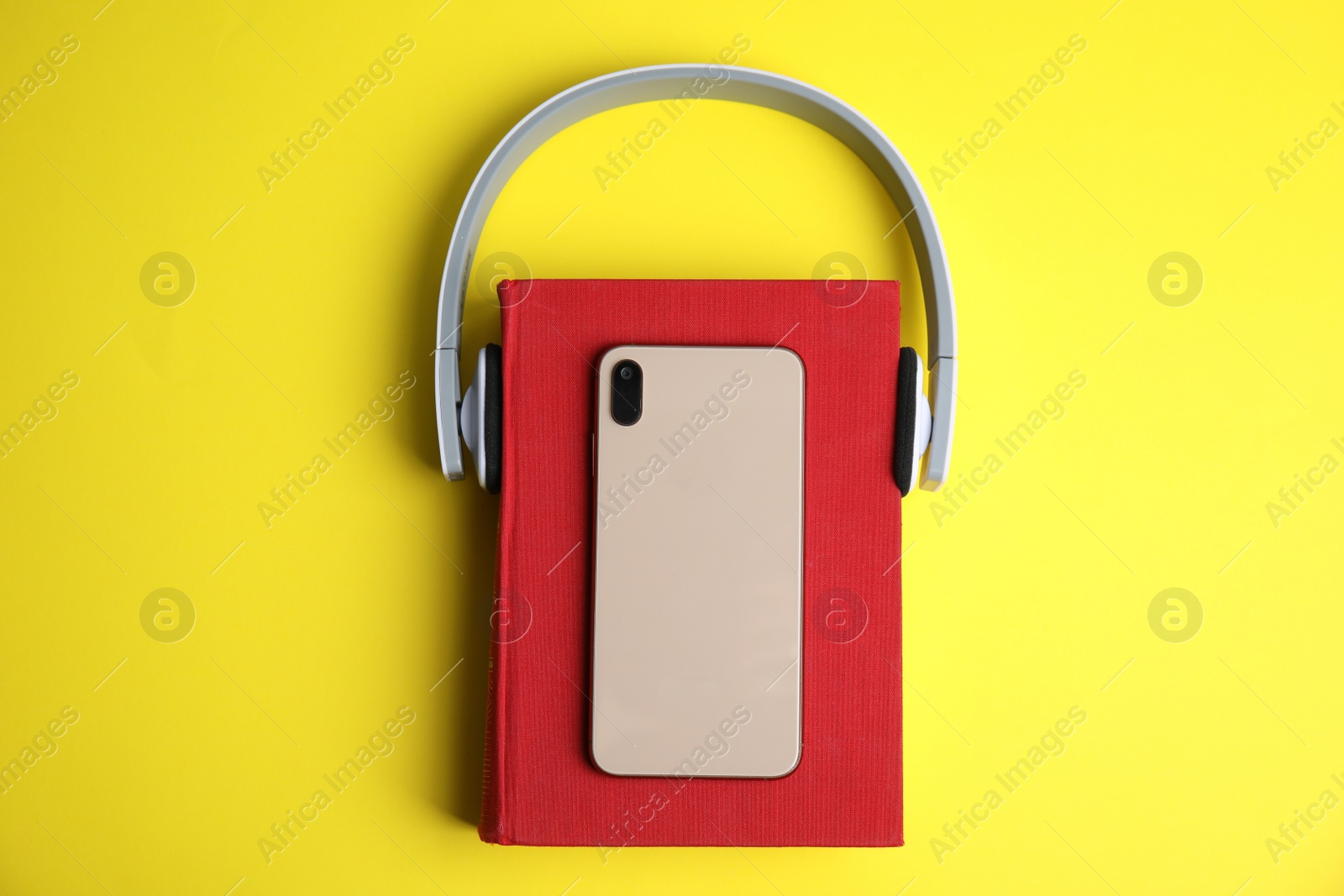 Photo of Book, modern headphones and smartphone on yellow background, top view