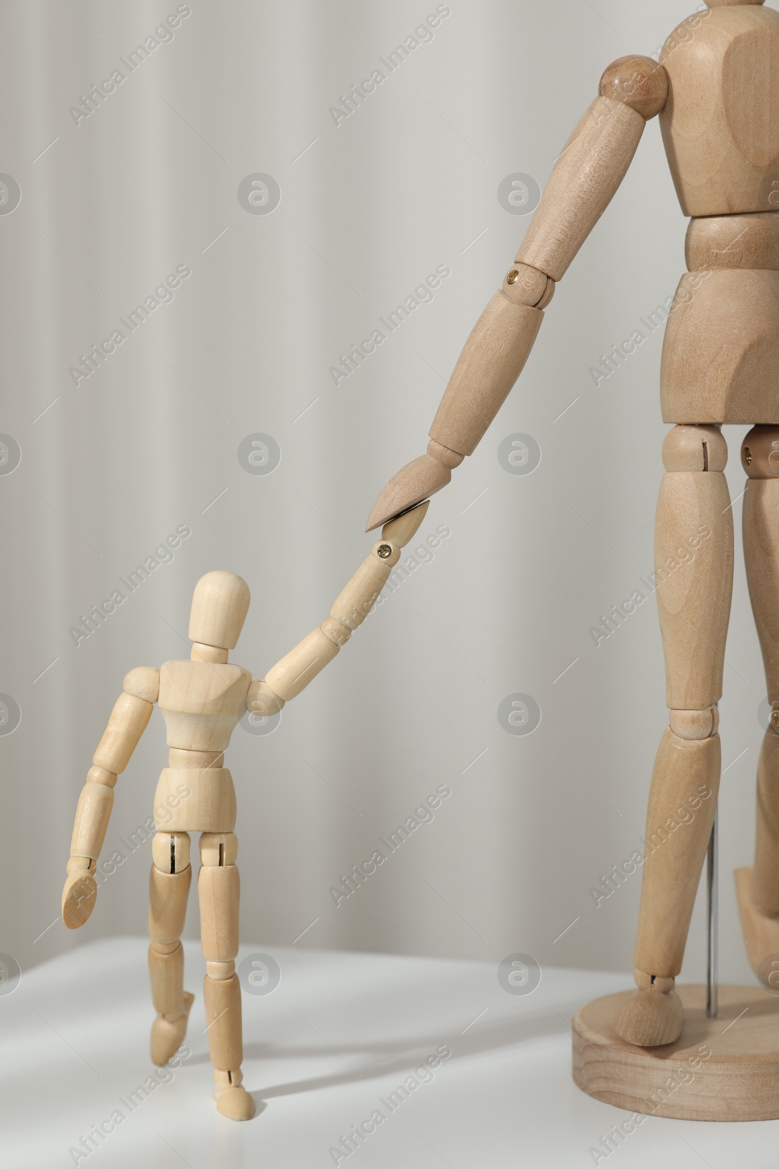 Photo of Wooden mannequins of parent with child on white table against light background. Family Day