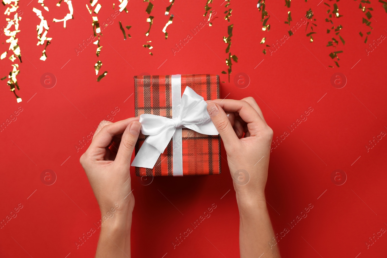 Photo of Woman with Christmas gift near gold confetti on red background, top view