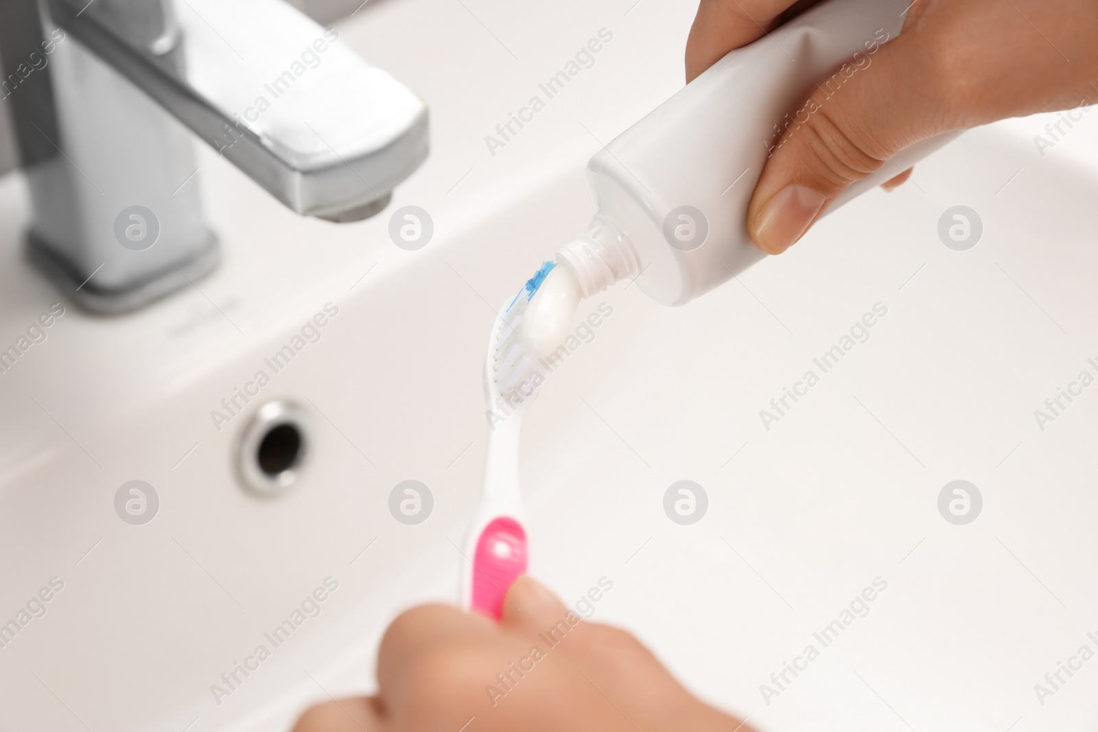 Photo of Woman applying toothpaste on brush in bathroom, closeup