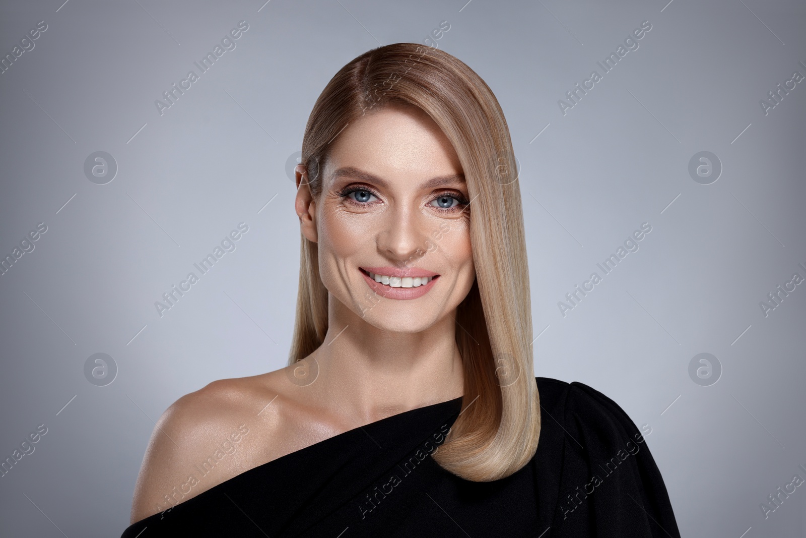 Image of Portrait of stylish attractive woman with blonde hair smiling on grey background