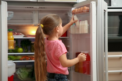 Cute little girl choosing food in refrigerator at home