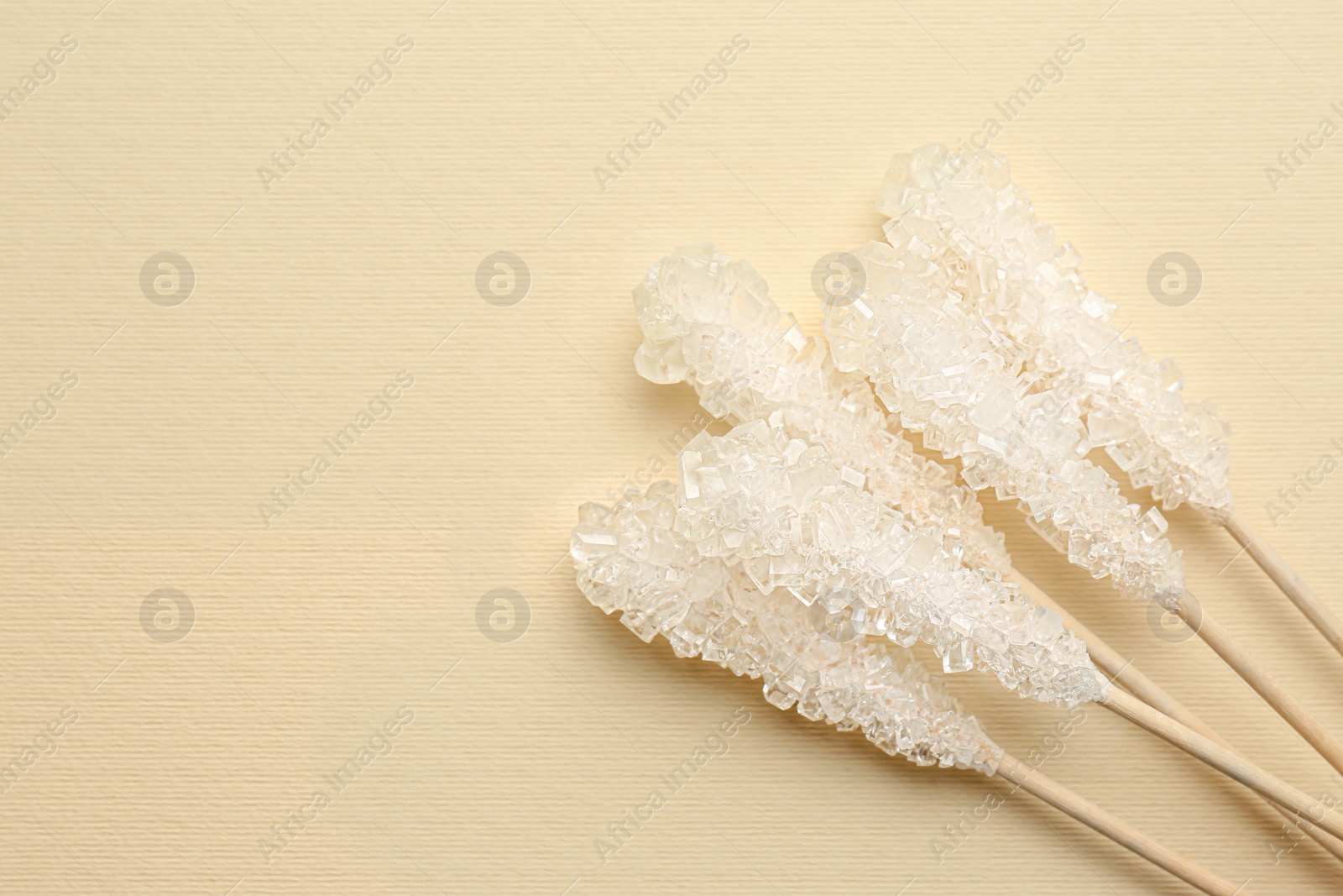 Photo of Wooden sticks with sugar crystals and space for text on beige background, flat lay. Tasty rock candies