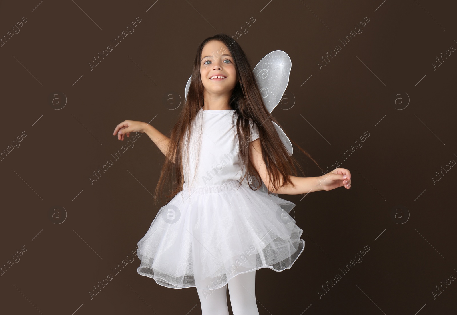 Photo of Cute little girl in fairy costume with white wings on brown background