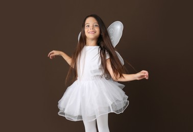 Photo of Cute little girl in fairy costume with white wings on brown background