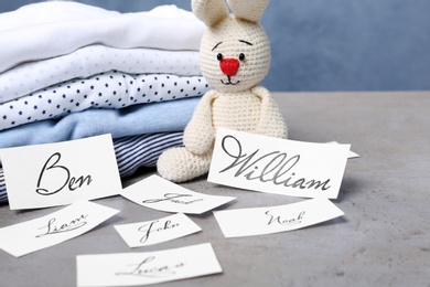 Photo of Paper sheets with different baby names, toy and child's clothes on grey table