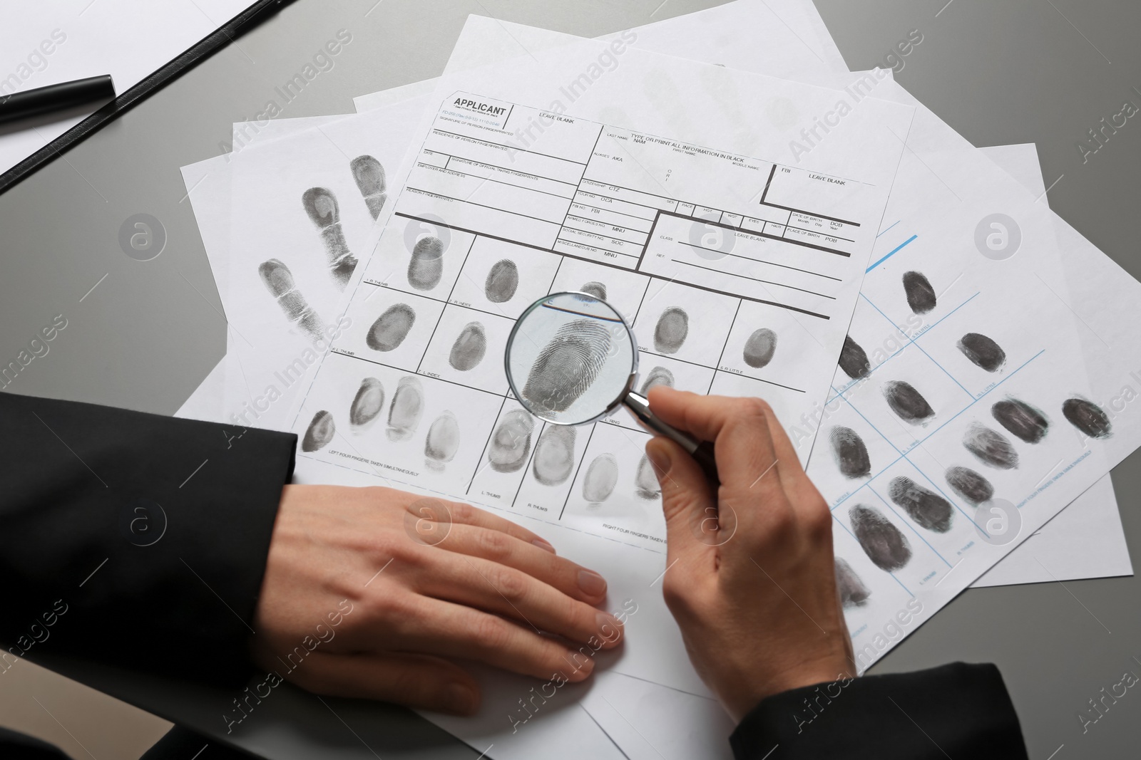 Photo of Female criminalist exploring fingerprints with magnifier at table, closeup