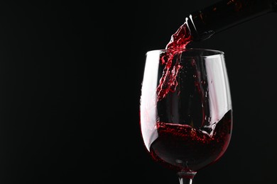 Photo of Pouring red wine into glass against black background, closeup. Space for text