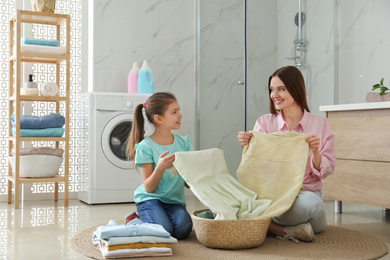 Mother and little daughter with clean laundry in bathroom