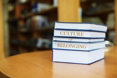Image of Stack of books with phrase Culture of Belonging on table in library. Space for text