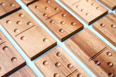 Photo of Wooden domino tiles on light blue background, closeup