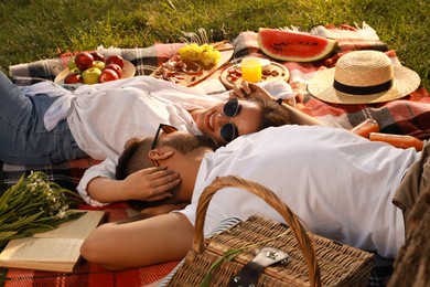 Happy young couple resting on picnic plaid outdoors