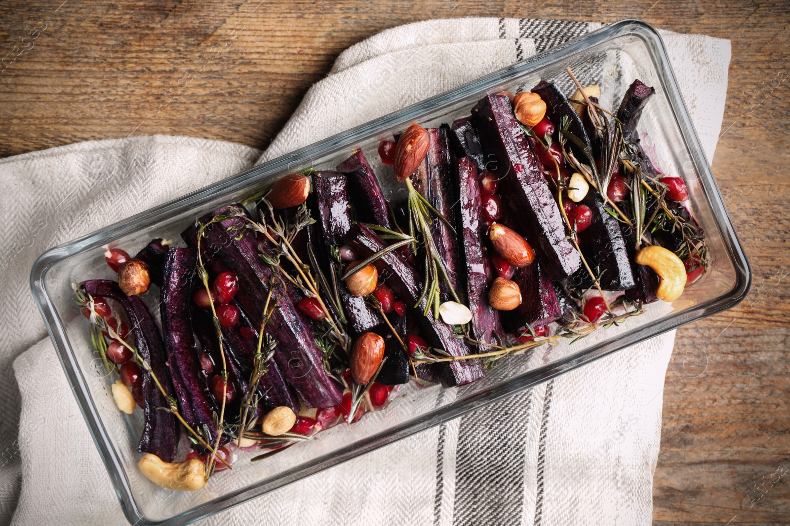 Photo of Baked black carrot with pomegranate seeds and nuts on wooden table, top view