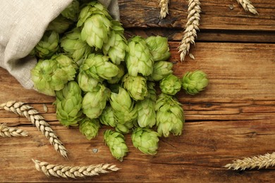 Sack with fresh green hops and wheat ears on wooden table, flat lay