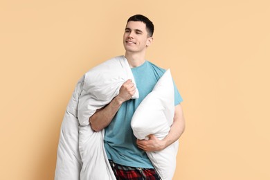 Happy man in pyjama holding pillow and blanket on beige background